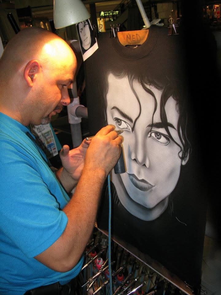 Efrain airbrushing a black and white celebrity portrait onto a T-shirt